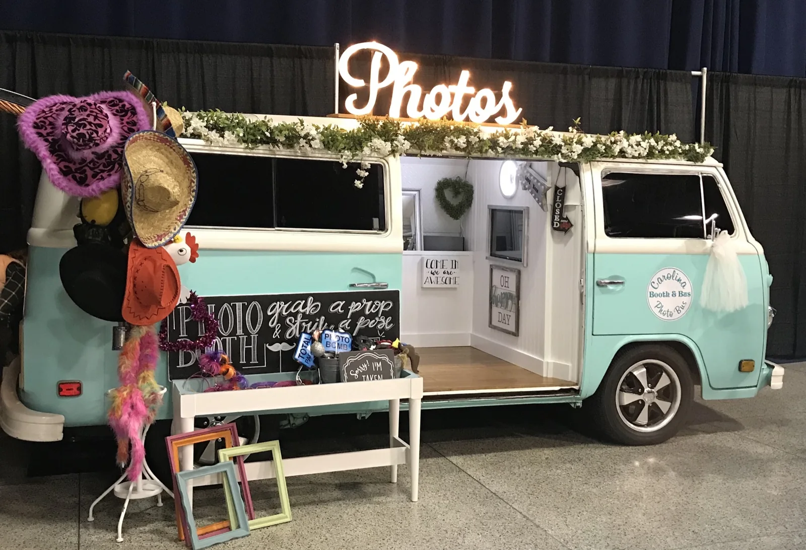 Lola, an aqua-and-white 1978 Volkswagen photo booth bus with the side door open and a glowing Photos sign.