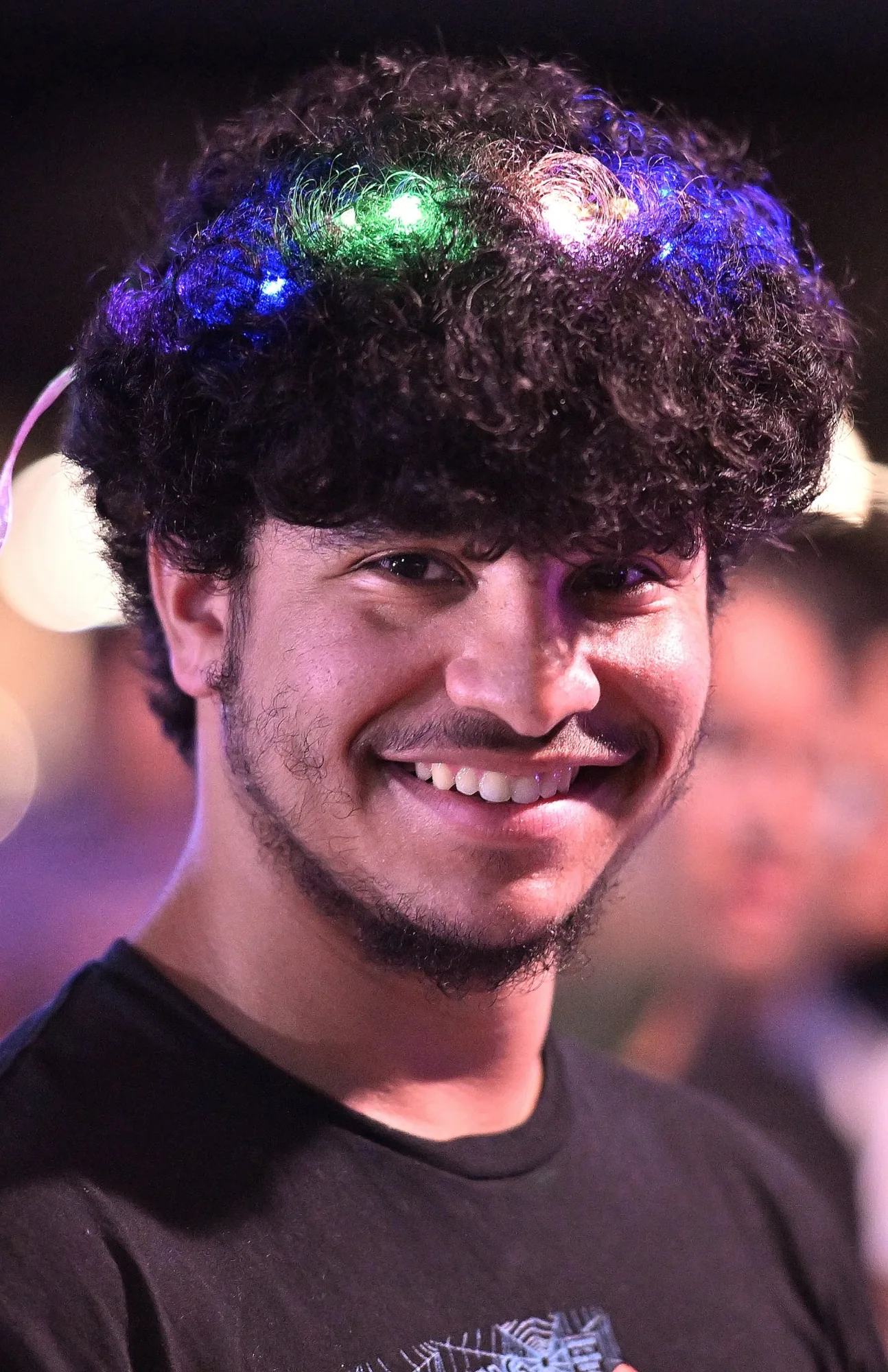 A student smiling with colorful lights woven into his hair at Noche de Disco.